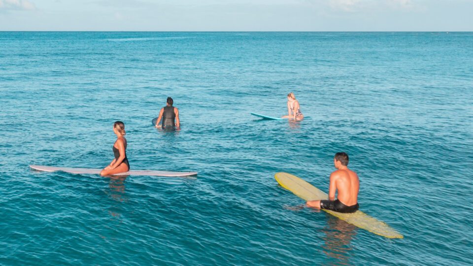 4 nois que fan surf longboard mediterrani, assegut esperant la onada, 2 nois i 2 noies surfistes